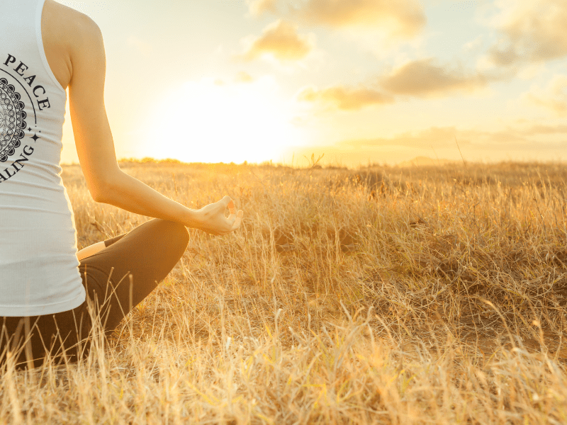 “A peaceful person meditating in nature at sunrise, surrounded by soft light and grounded energy—symbolizing the release of trapped emotions and the journey to self-compassion.”