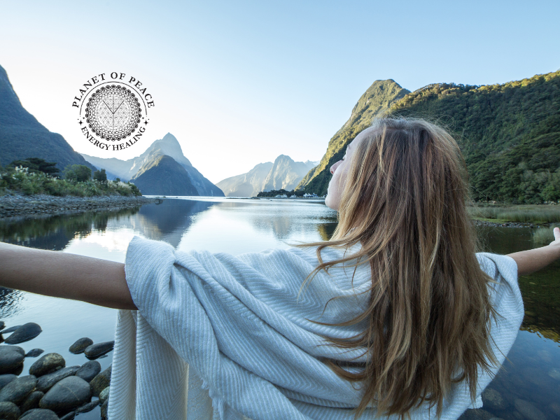 Woman standing peacefully by a river with arms open, symbolizing the emotional release of stubbornness and the flow of healing energy.